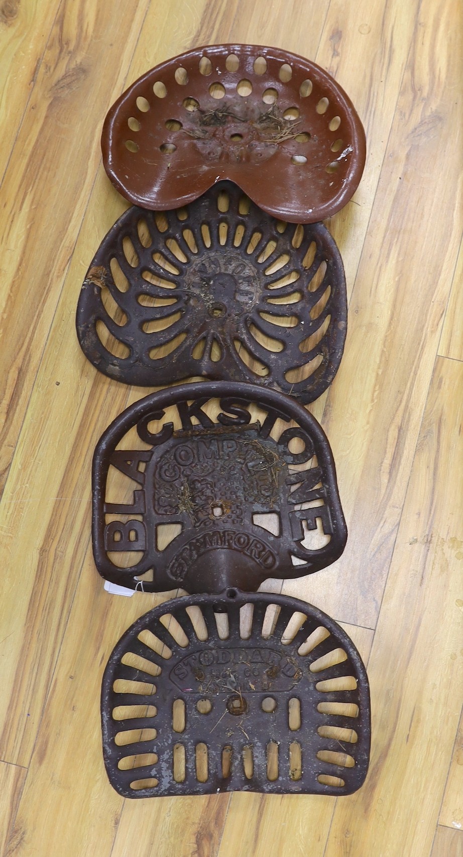 Four assorted cast iron and enamelled tractor seats